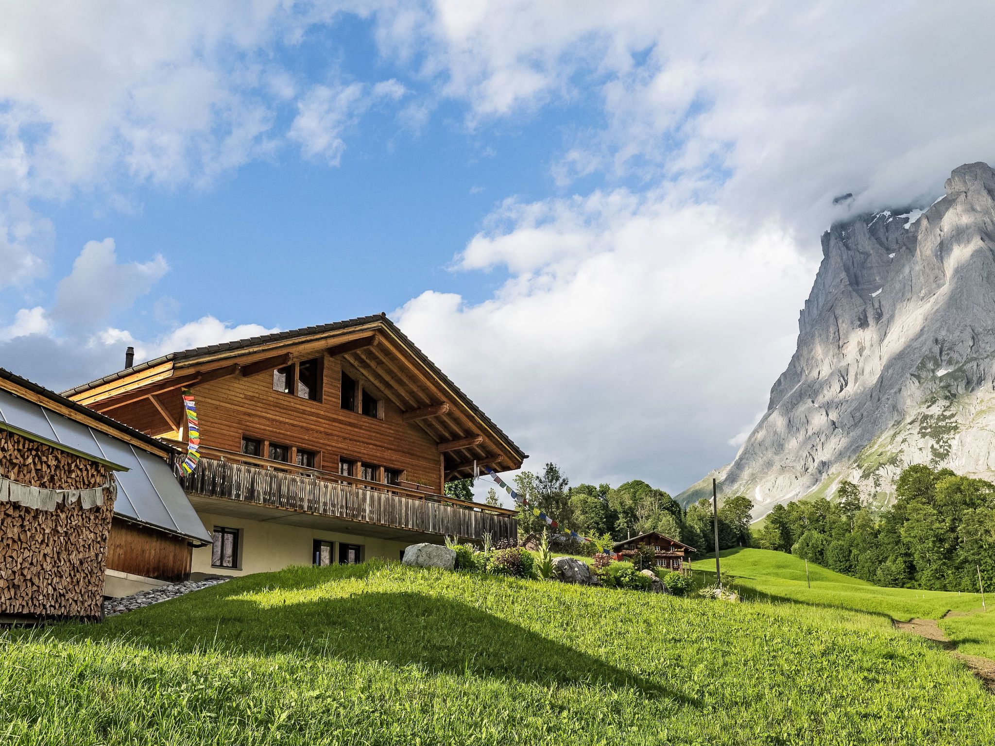 Un chalet en bois doté d’un balcon donnant sur un champ verdoyant et, au loin, sur une montagne.