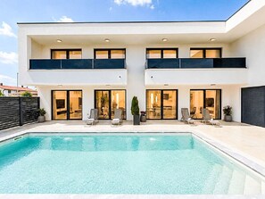 Una casa moderna de dos pisos con piscina, ventanas amplias y zona de estar al aire libre.