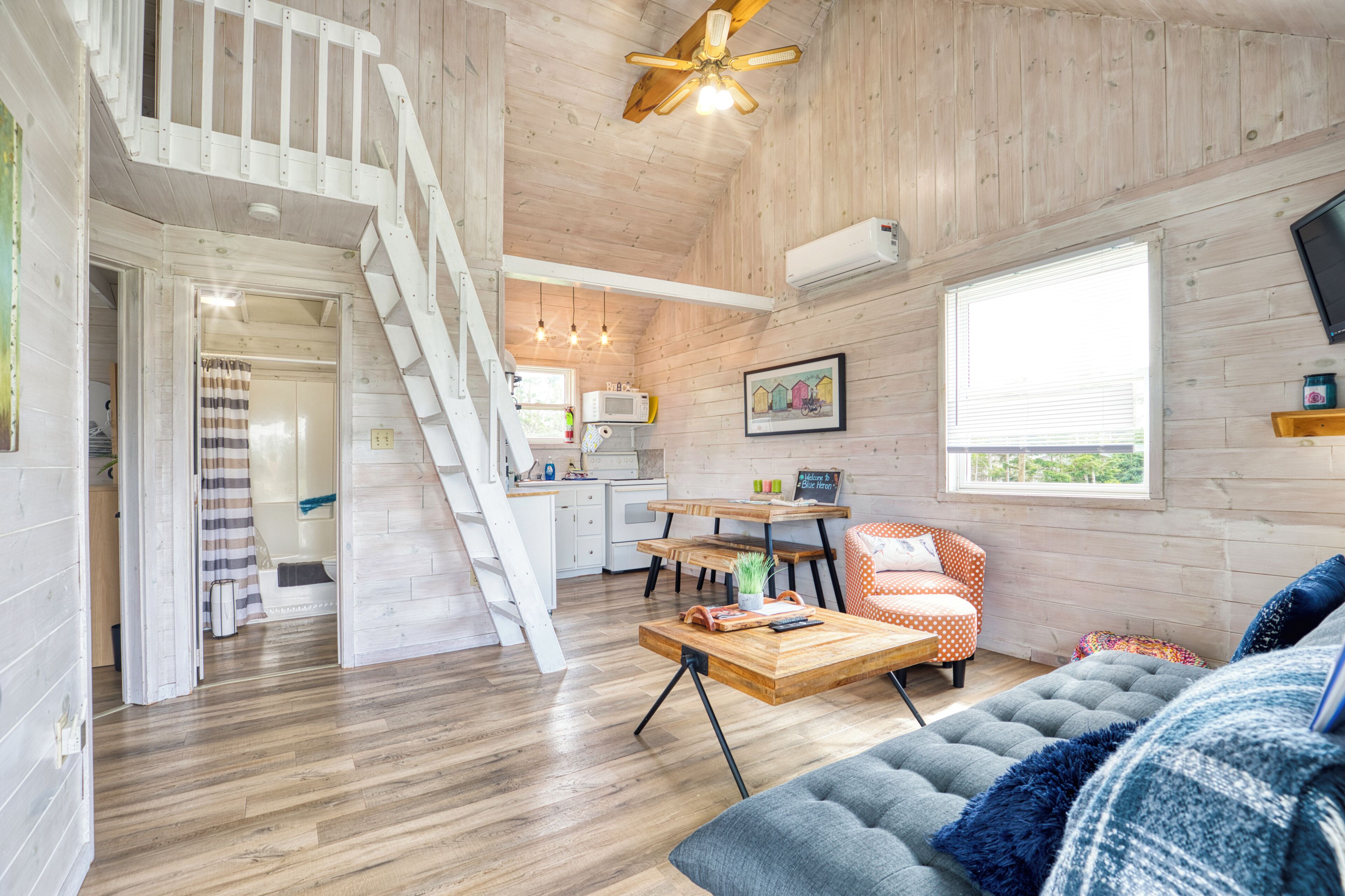 A spacious living area with a staircase, wooden floors, a sofa, a coffee table, and a kitchen in the background.