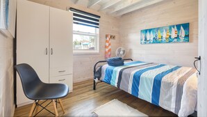 Ein Schlafzimmer mit einem Bett, einem Sessel, einem Kleiderschrank, einem Gemälde und einem Fenster mit Jalousien.