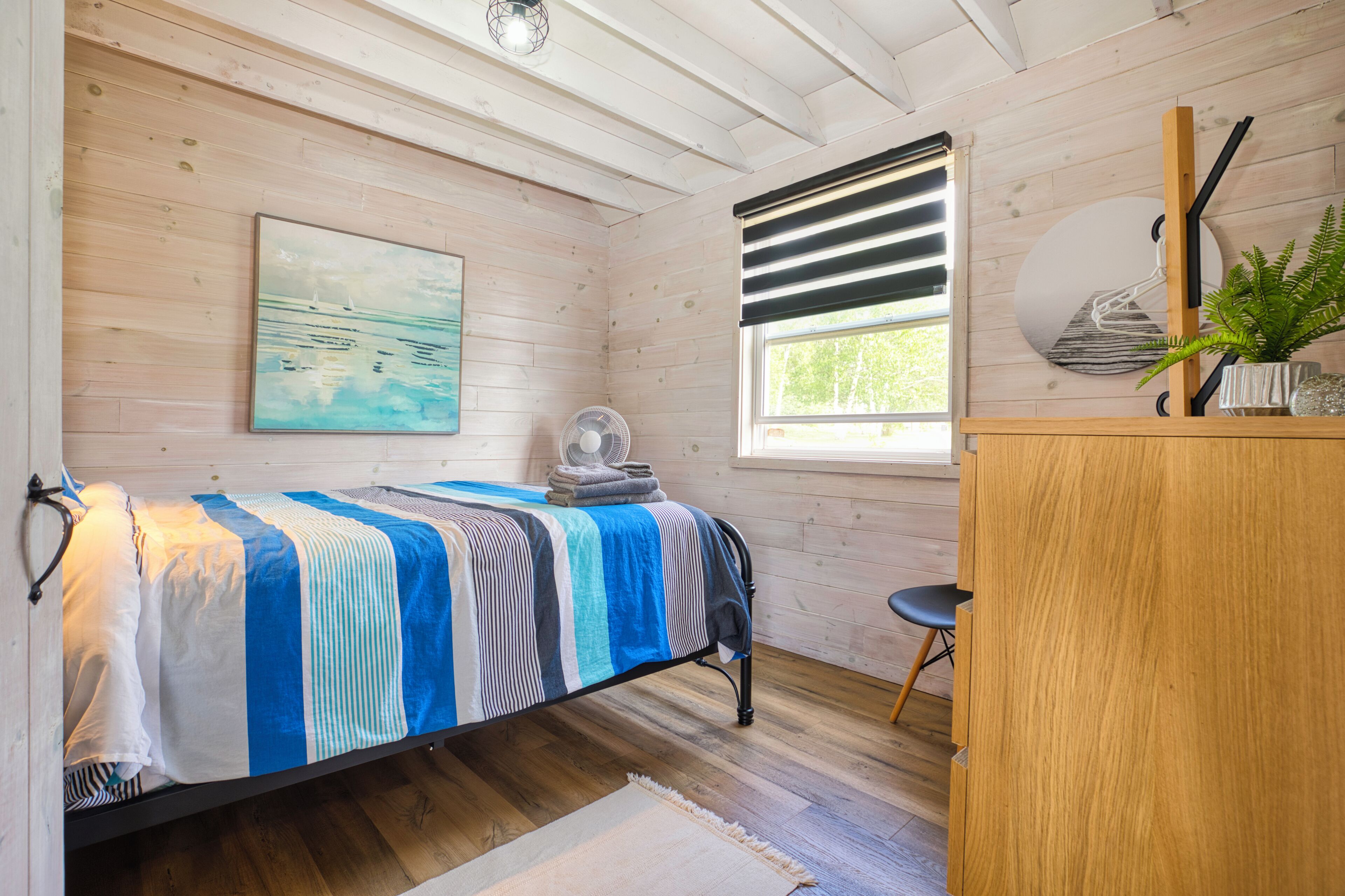 Une chambre à coucher avec un lit, un bureau, un ventilateur et une fenêtre avec des stores.