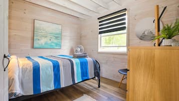 Une chambre à coucher avec un lit, un bureau, un ventilateur et une fenêtre avec des stores.