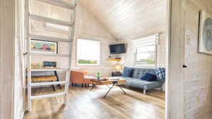 Ein gemütlicher, gut beleuchteter Raum mit Holzbalkendecke, einer Couch, einem Couchtisch und einem an der Wand befestigten Fernseher.