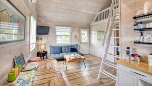 Ein gemütliches Blockhaushaus-Interieur mit Holzboden, einer Couch, einem Esstisch und einer Leiter zu einem Schlafboden.