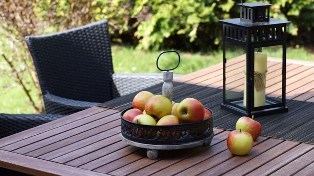 A wooden table with a bowl of apples and a black lantern. - Vacation home Marcel by Interhome (Hage)