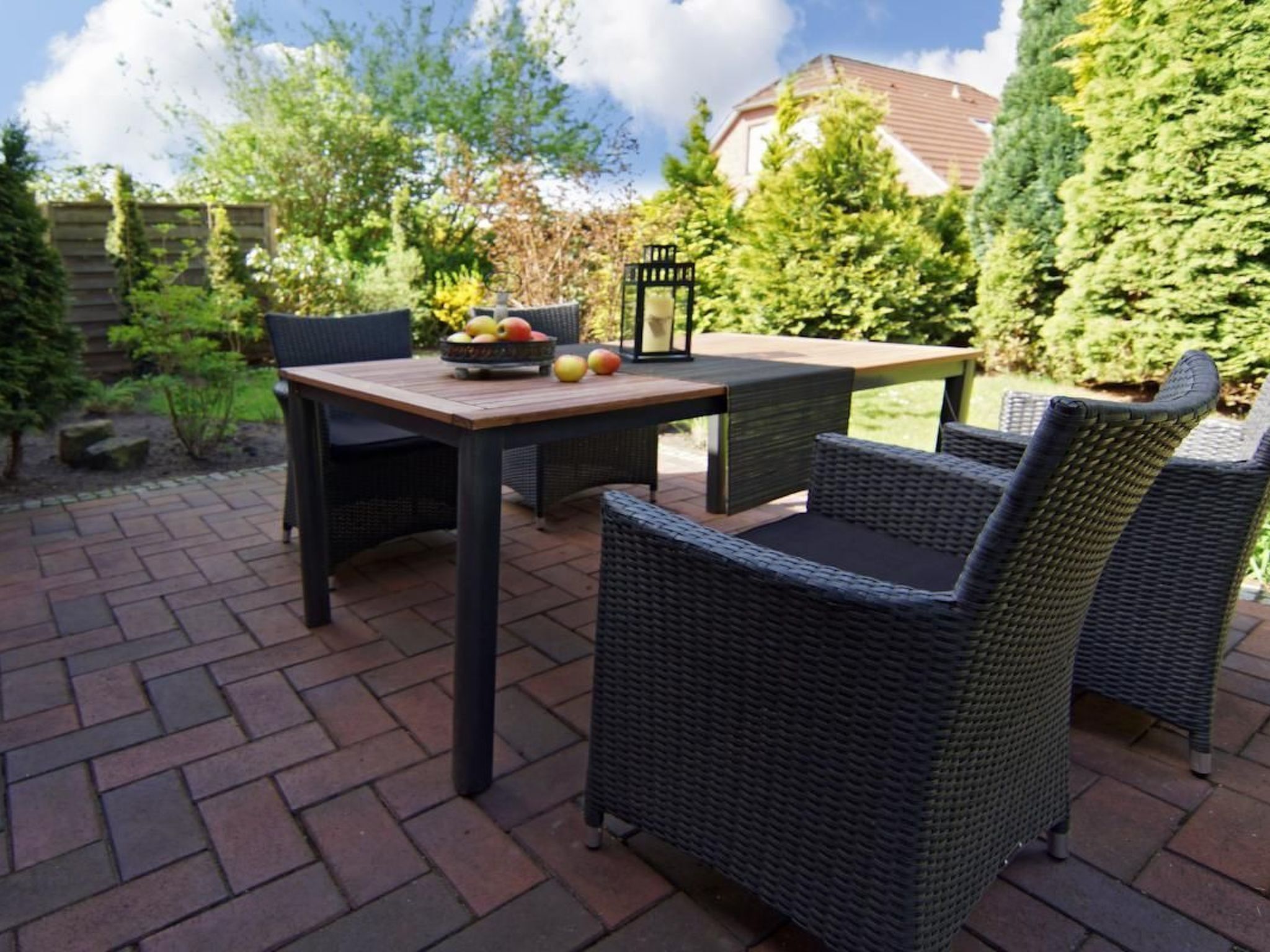 An outdoor patio area with a table and two wicker chairs, a bowl of fruit, and a lantern.