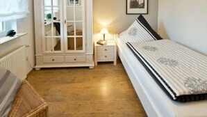 A bedroom with a bed, a white wardrobe, a nightstand, a lamp, and a framed picture on the wall. - Vacation home Marcel by Interhome (Hage)