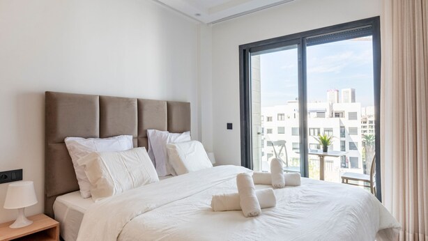 A modern hotel room with a large bed, a nightstand, and a view of the city through a large window. - Charmante Wohnung 42 by Interhome (Casablanca)