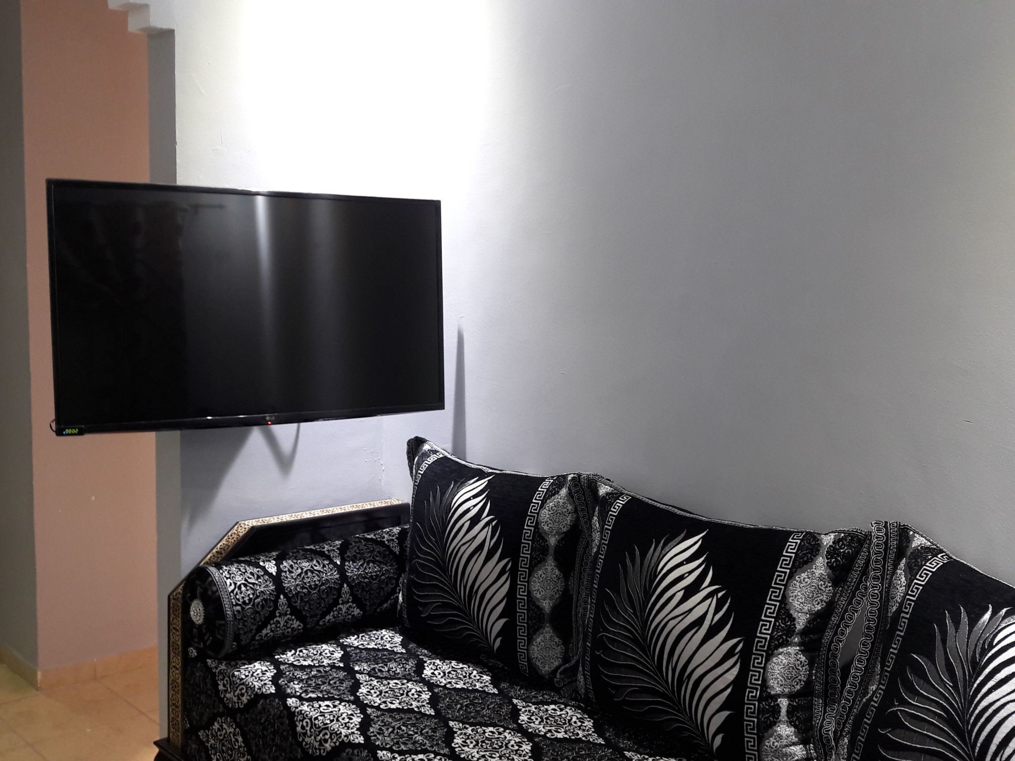 A living room with a black sofa featuring white leaf patterns, a flat-screen TV mounted on the wall, and a light-colored floor.
