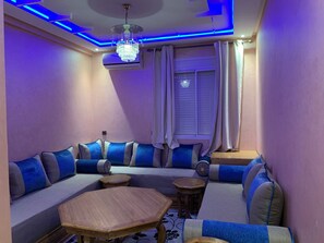 Un salon moderne avec un canapé d’angle, une table basse en bois et un lustre.