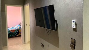Ein Flur mit einem an der Wand montierten Fernseher, einem Thermostat und einer Tür zu einem Zimmer mit einem Bett.