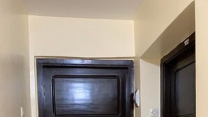 Eine dunkle Holztür mit Metallbeschlägen und Schlüsselloch, platziert in einem Korridor mit beige gestrichenen Wänden und Fliesenboden.