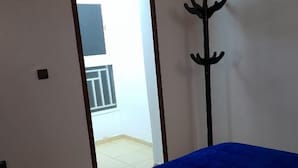 A room with a bed covered in a blue blanket, a coat rack, and a door leading to an outdoor balcony. - Résidence Annasr 1 by Interhome (Agadir)