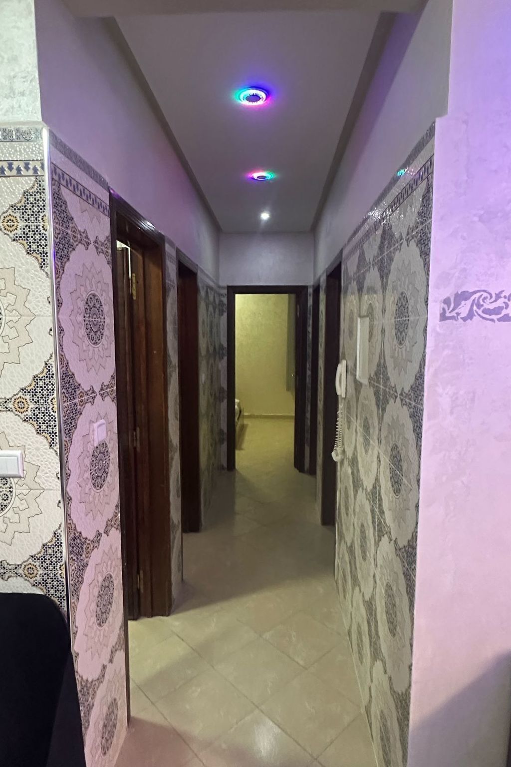 A hallway with patterned walls and a tiled floor, leading to a room with a door.