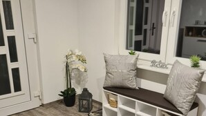 Ein modernes Wohnzimmer mit Holzboden, einem grauen Teppich, einem weißen Sofa mit Stauraum, einer kleinen Pflanze und einem Fenster mit Blick.