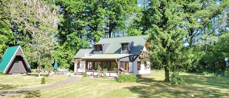 A two-story house with a green roof, surrounded by a grassy lawn and trees.