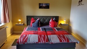 Une chambre à coucher comprenant un lit, deux lampes de chevet, un radiateur, une fenêtre avec des rideaux et un tableau accroché au mur.