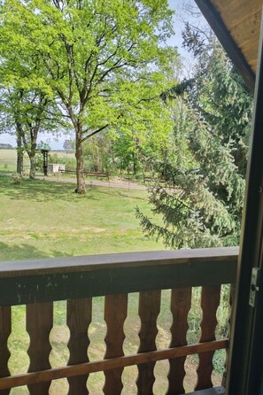 A view from a balcony with a wooden railing, overlooking a grassy area with trees and a small structure. - Itzinger by Interhome (Ziesar)