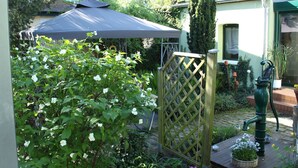 Ein Garten mit Holzzaun, einer Wasserpumpe und einem überdachten Bereich mit Tisch.
