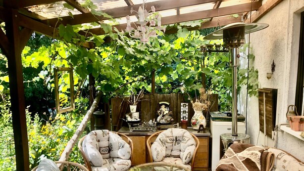 Ein gemütlicher Außenbereich mit Korbmöbeln, einem Glastisch und einer Holzpergola.