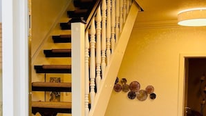 Una escalera con barandillas blancas y peldaños oscuros, que conduce a una habitación con piso de madera y un adorno en la pared.