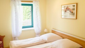 Een slaapkamer met een bed, een raam met gordijnen, een lamp en een ingelijst schilderij aan de muur.