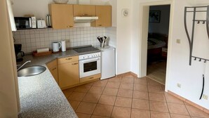 Een compacte keuken met een magnetron, broodrooster en koffiezetapparaat op het aanrecht, een spoelbak en een fornuis.