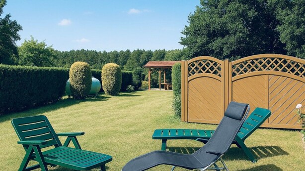 Een tuin met gazon, houten omheining en een tuinhuis.
