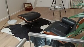 Una sala de estar moderna con un sofá de cuero negro, una mesa de centro de cristal, una lámpara de pie y un trípode.