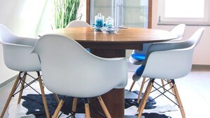 Un comedor con mesa de madera, sillas blancas, alfombra blanco y negro y una lámpara colgante grande.