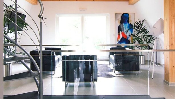 Un interior moderno con una escalera, una mesa de vidrio y una pintura.