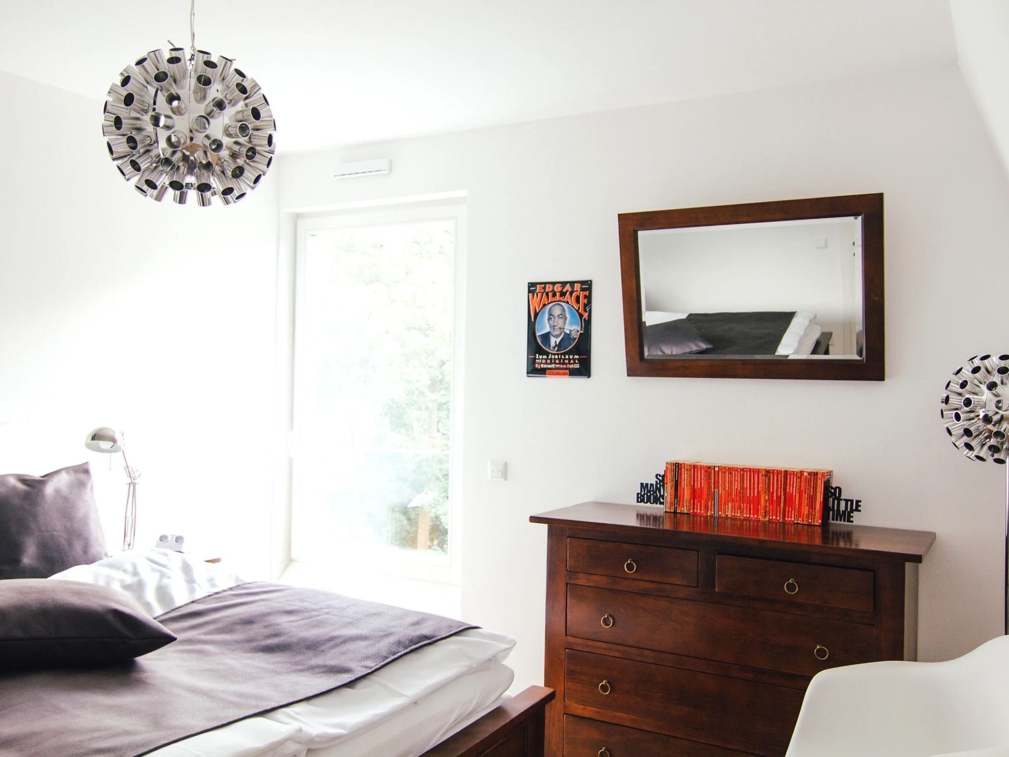 A bedroom with a bed, a dresser, a mirror, and a hanging light fixture.