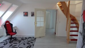 A room with a red gaming chair, a patterned rug, a wooden staircase, and a door leading to another room. - Rotkehlchenweg by Interhome (Bannesdorf)