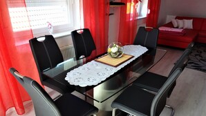 A dining area with a glass table, black chairs, a lace table runner, and a red sofa in the background. - Rotkehlchenweg by Interhome (Bannesdorf)