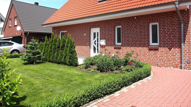 A two-story brick house with a red-tiled roof, a garage, and a well-maintained garden with hedges and flowers. - Rotkehlchenweg by Interhome (Bannesdorf)