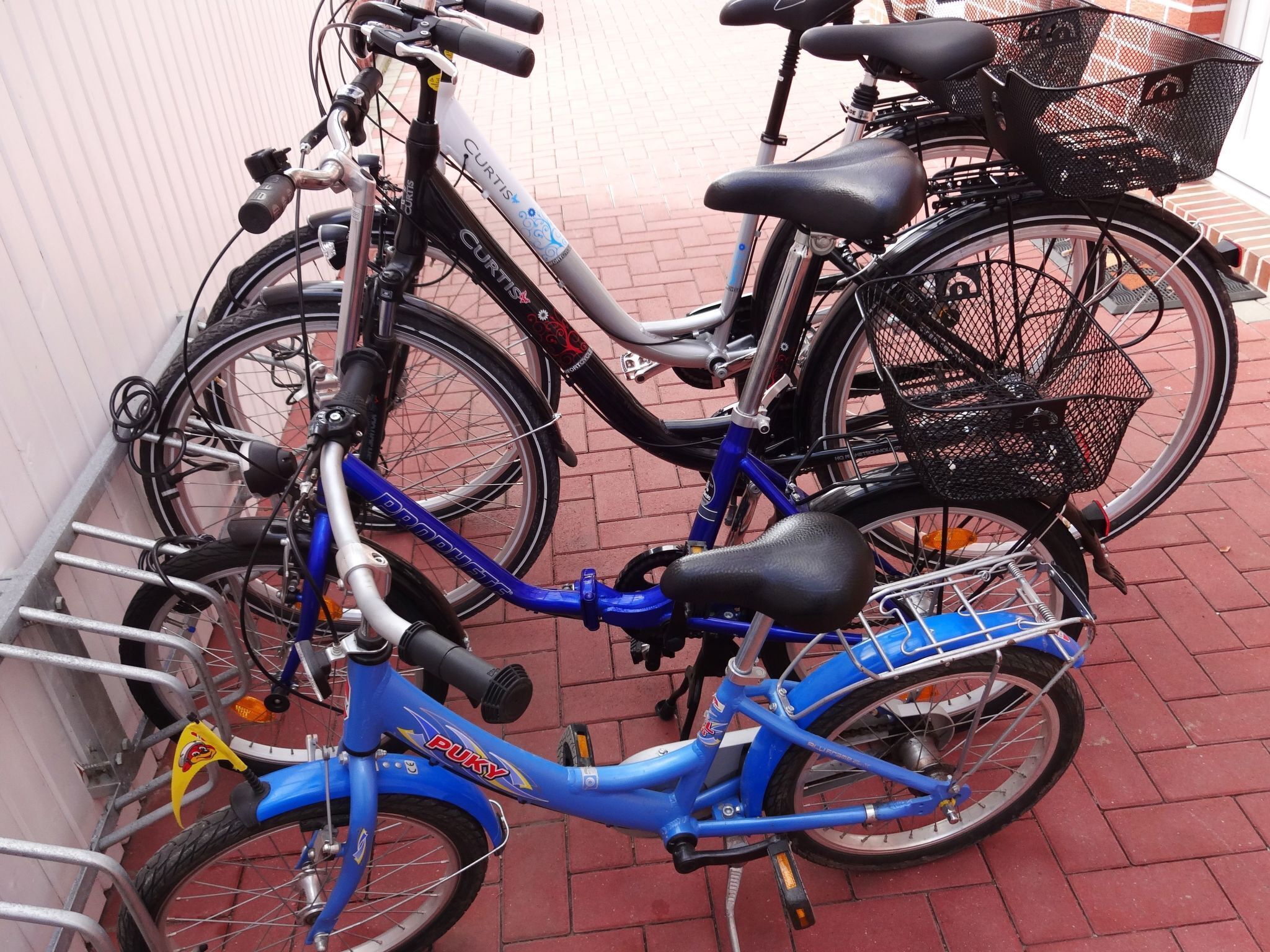 A blue bicycle with a basket and a black seat, parked next to a white bicycle with a black basket.