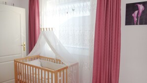 A room with a wooden crib, white walls, a window with sheer curtains, and a door with a golden handle. - Rotkehlchenweg by Interhome (Bannesdorf)