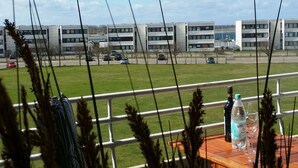 Vista de uma varanda com guarda-corpo, com vista para um estacionamento e edifícios modernos.