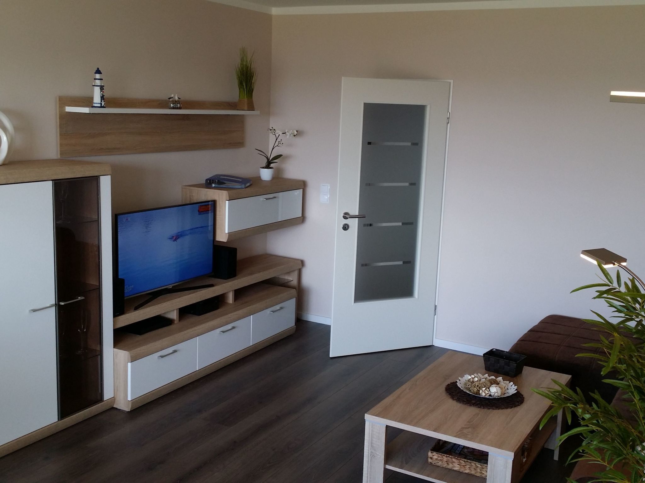 Un soggiorno moderno con una TV a schermo piatto, mobili in legno, una porta in vetro e un tavolino con oggetti decorativi.