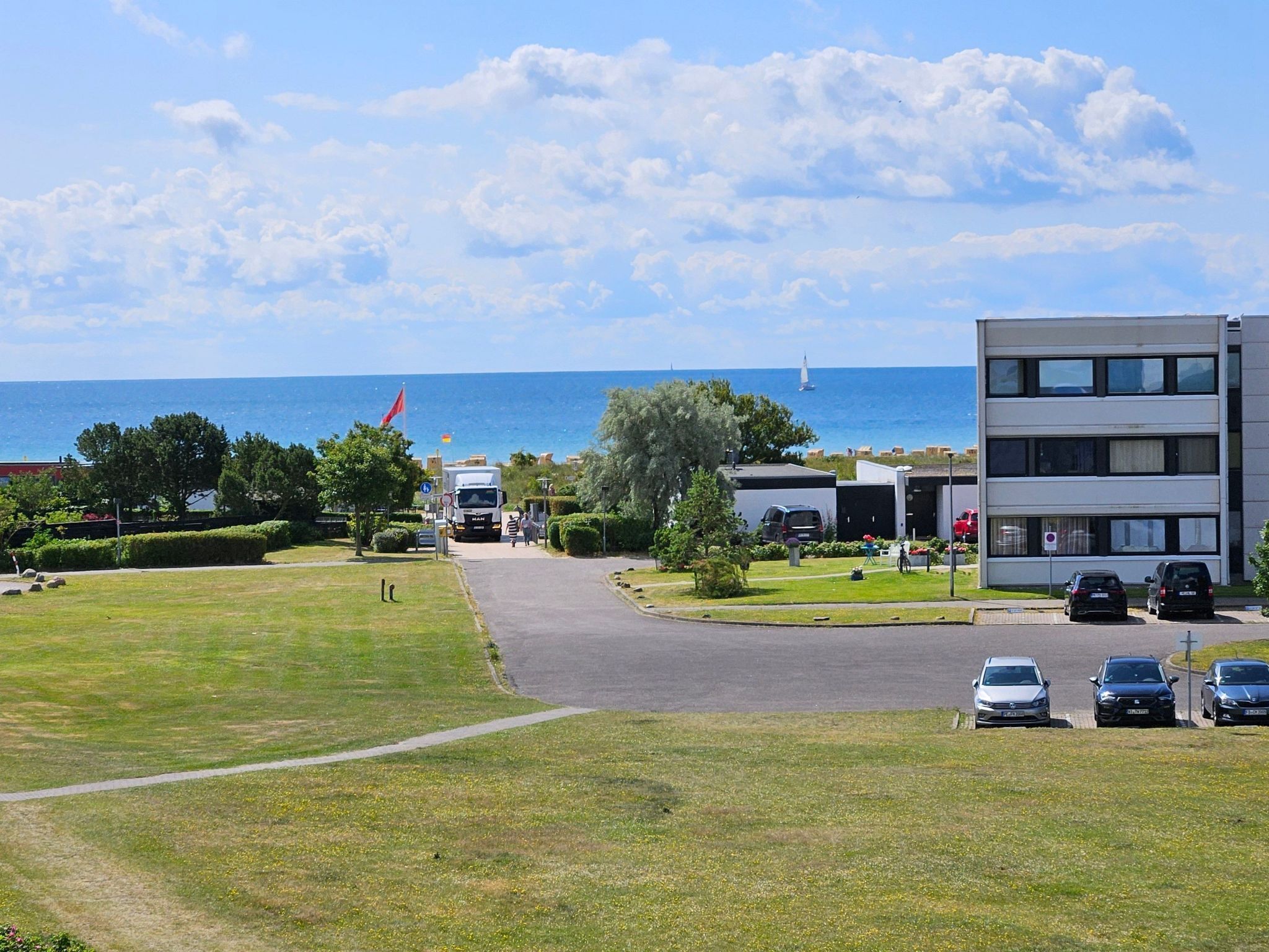 A coastal hotel with a parking area, a grassy lawn, and a view of the sea.