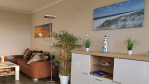 Uma sala de estar com um sofá marrom, um armário branco, um abajur e duas plantas em vasos.