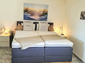 A bed with two pillows, a bedside table with a lamp, and a wall-mounted picture. - Strandurlaub im Ferienappartement mit Garten by Interhome (Heiligenhafen)