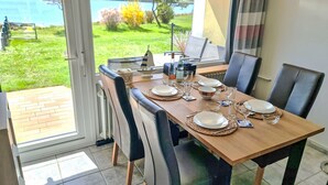 Comedor con una mesa dispuesta para cuatro personas, sillas, vista a un lago y un reloj en la pared.