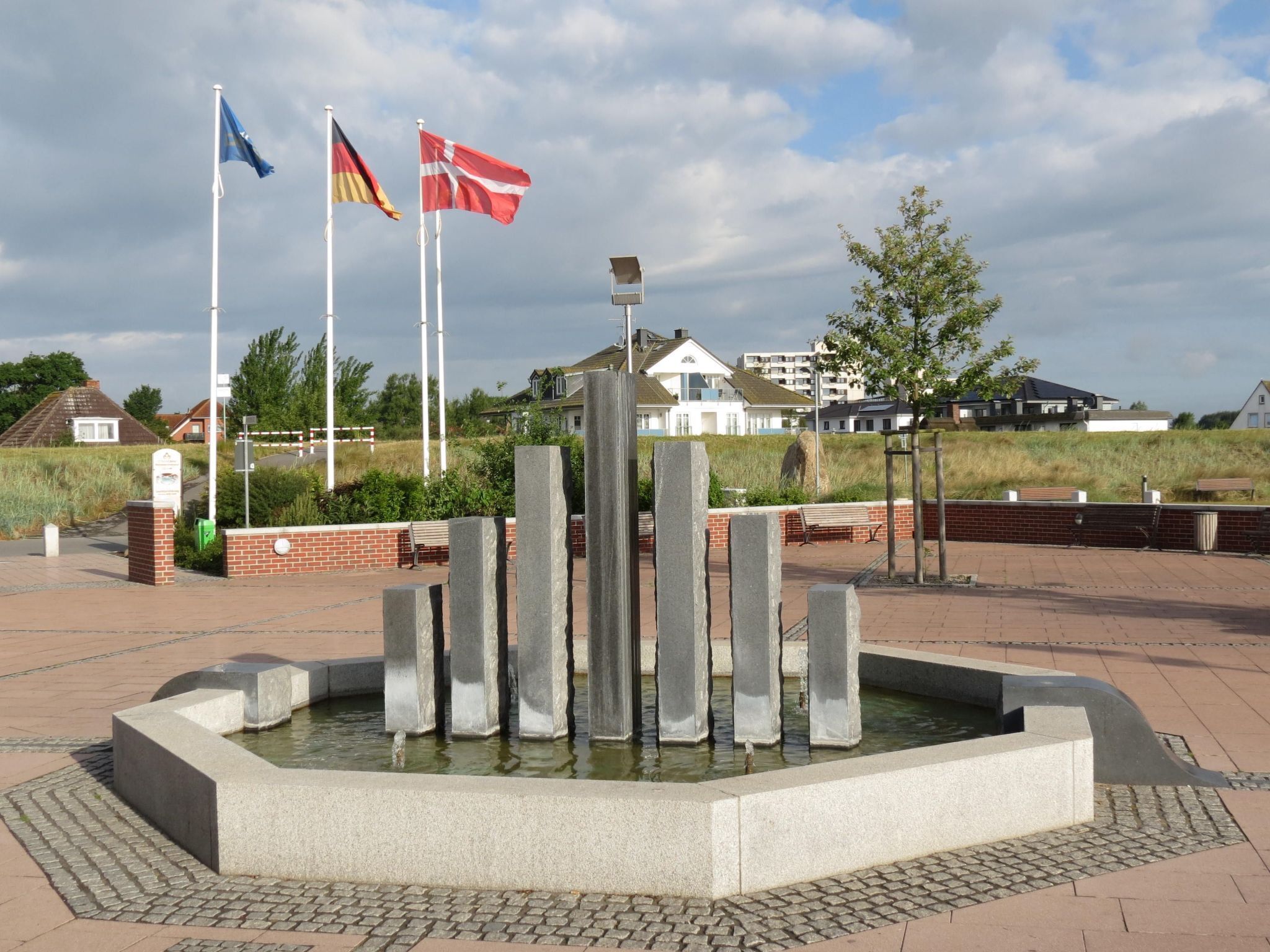 Een openbaar plein met een centrale fontein, banken en vlaggen.