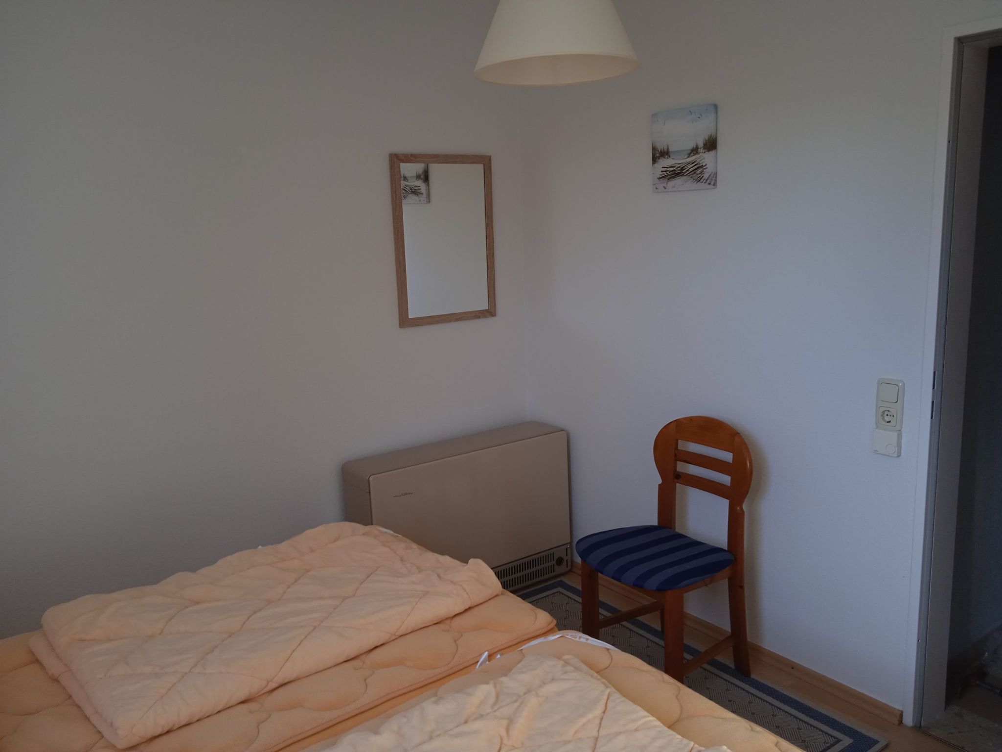A bedroom with a bed, a chair, a radiator, and a wall-mounted mirror.