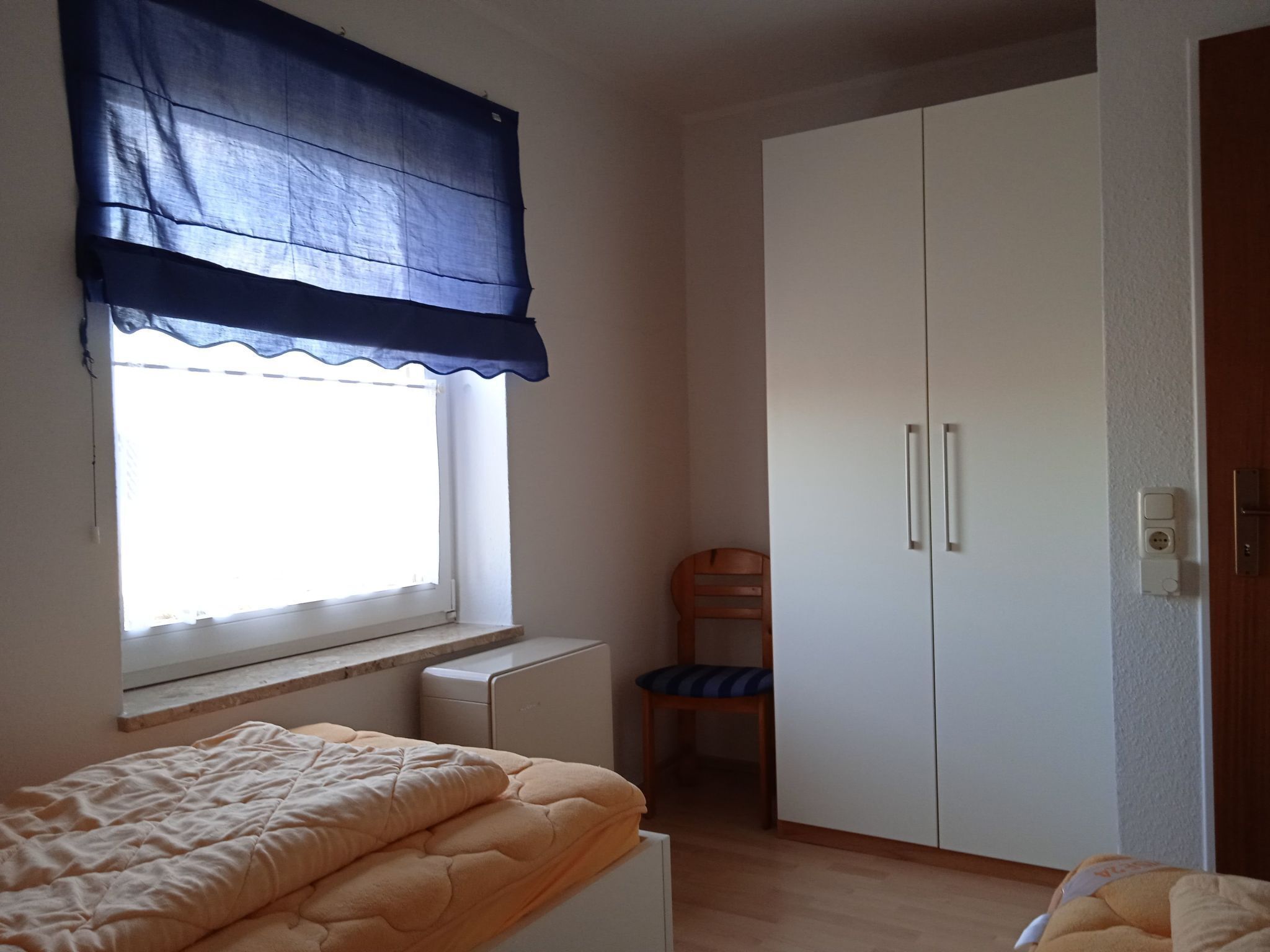 Um quarto com cama, cadeira, guarda-roupa e janela com cortina azul.