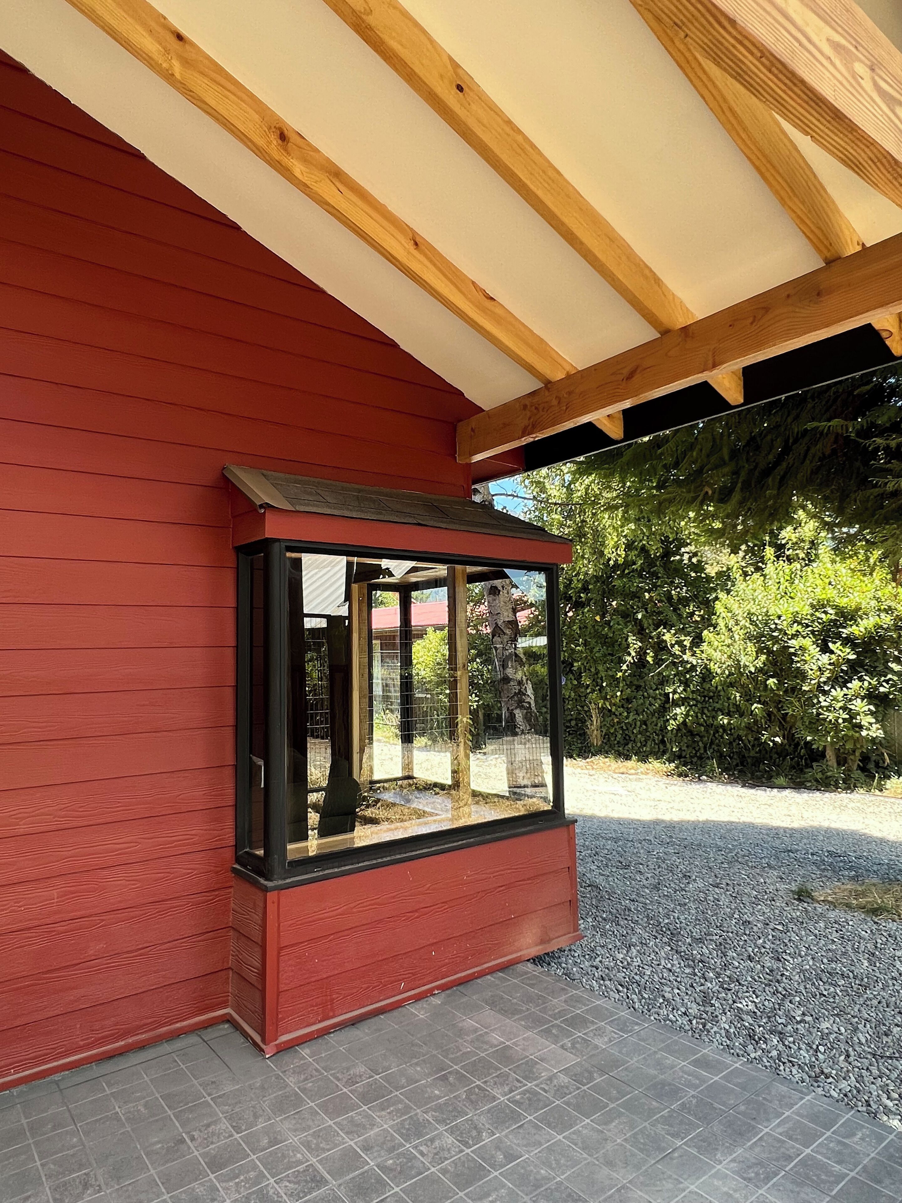 A red building with a glass enclosure, wooden beams, and a gravel path.