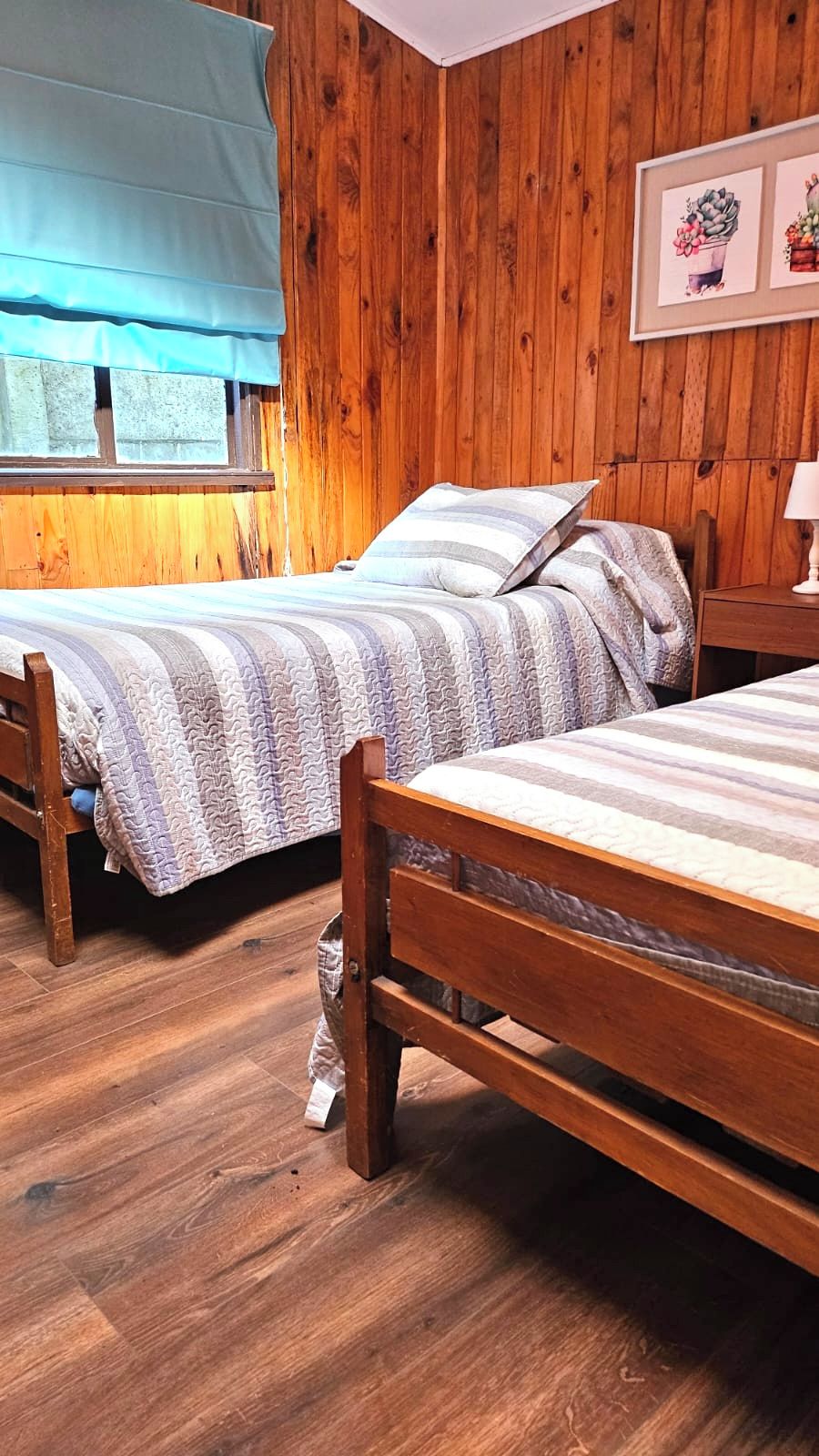 A room with two wooden beds, a window with a blue curtain, and wooden walls.