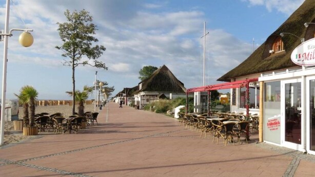 A seaside promenade with outdoor seating and a restaurant with a red awning. - Körner Kornhof 7 EG by Interhome (Dahme)