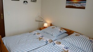 A bedroom with two beds, a nightstand, a wall-mounted lamp, and a painting of a sunset over the ocean. - Körner Kornhof 7 EG by Interhome (Dahme)